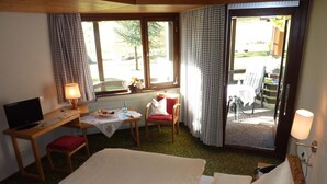 Une chambre d’hôtel avec un lit, un bureau avec un ordinateur, une chaise, une petite table avec un saladier de fruits et une vue sur l’extérieur.
