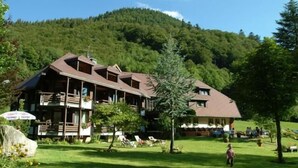 Un bâtiment de style chalet, doté d’un toit en pente, entouré d’une pelouse verdoyante et luxuriante et d’arbres.
