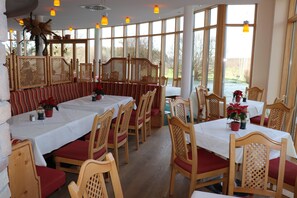 A restaurant with wooden furniture, white tablecloths, and large windows offering a view of the outdoors. - Wengerhof (Ainring)