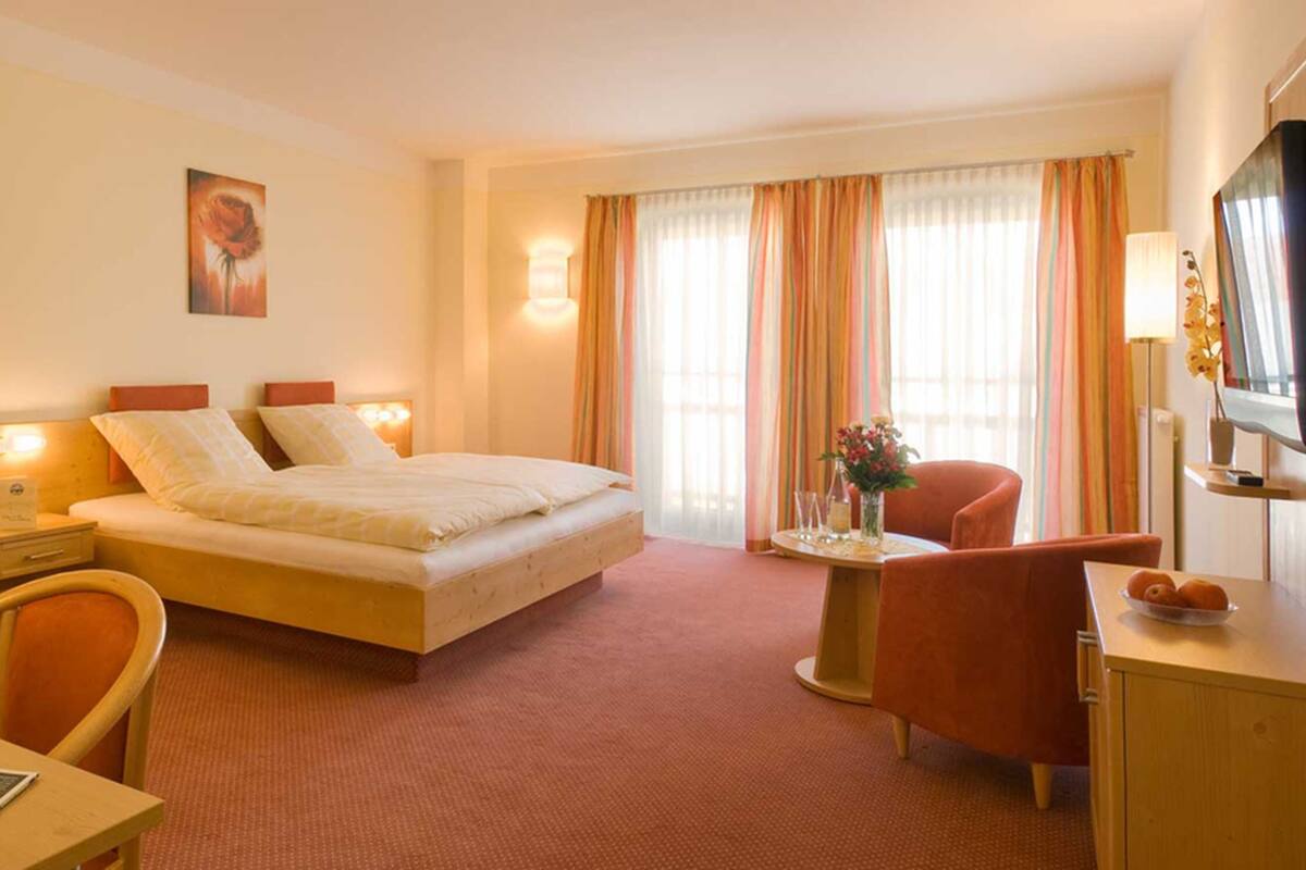 A hotel room with a bed, a desk, a chair, a TV, and a window with curtains.