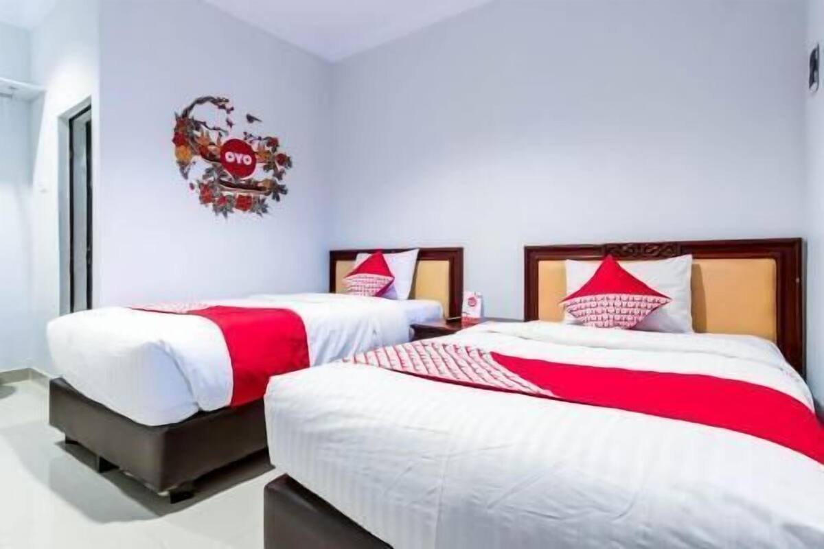 A hotel room with two beds, each with white bedding and red accents, a wall decoration, and a door.