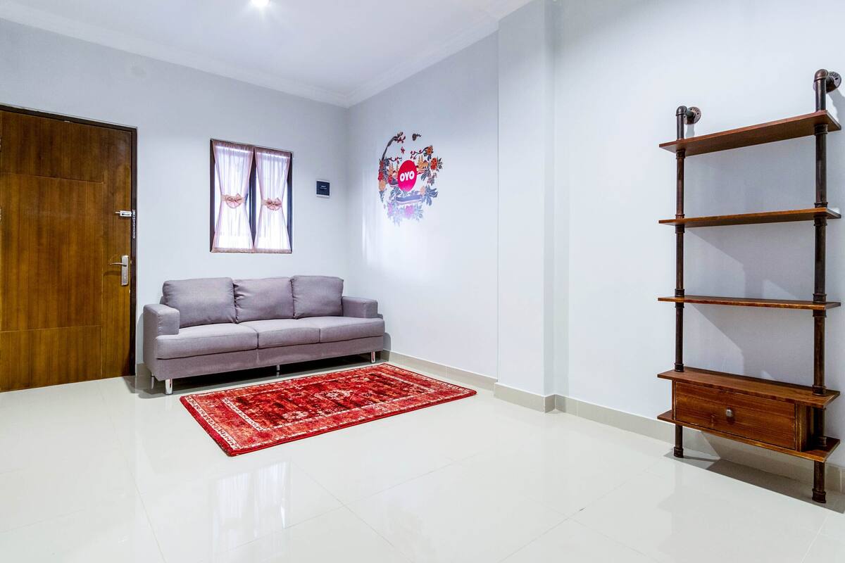 A living room with a grey sofa, a red rug, a wooden shelf, and a door.