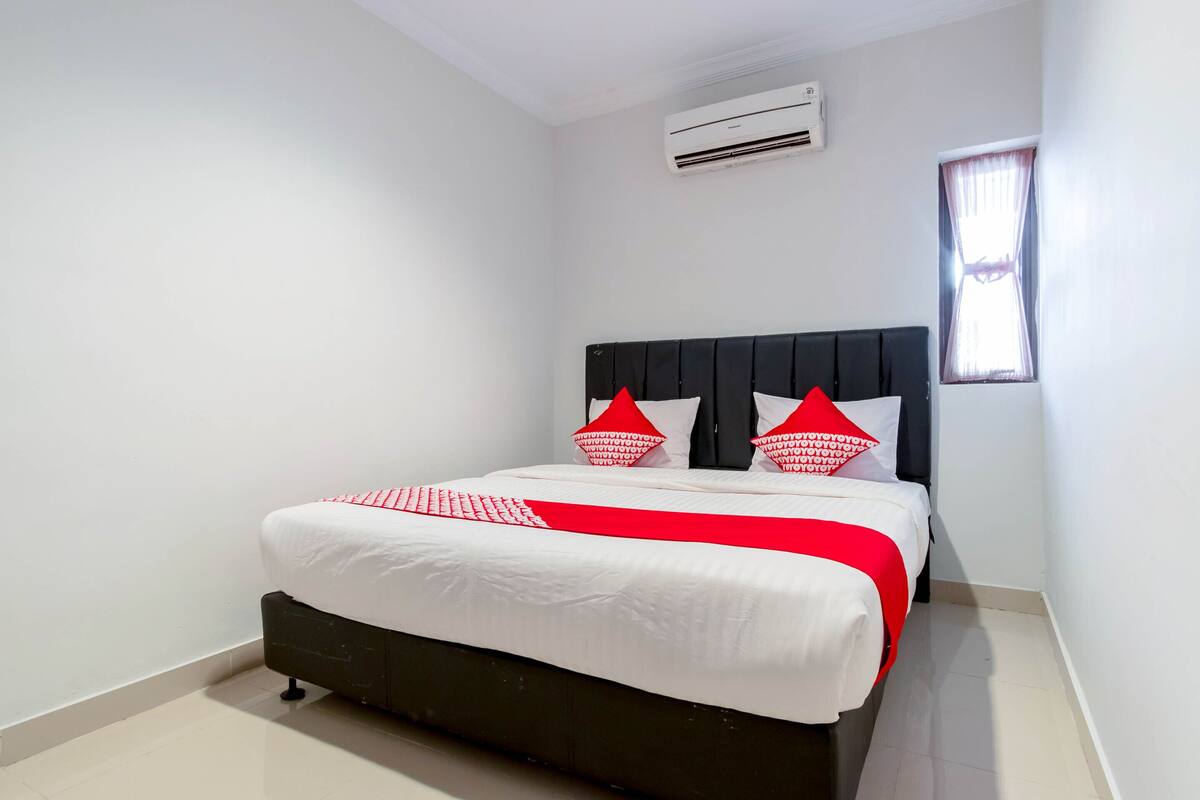 A neatly made bed with white and red bedding, a black headboard, and a window with curtains.