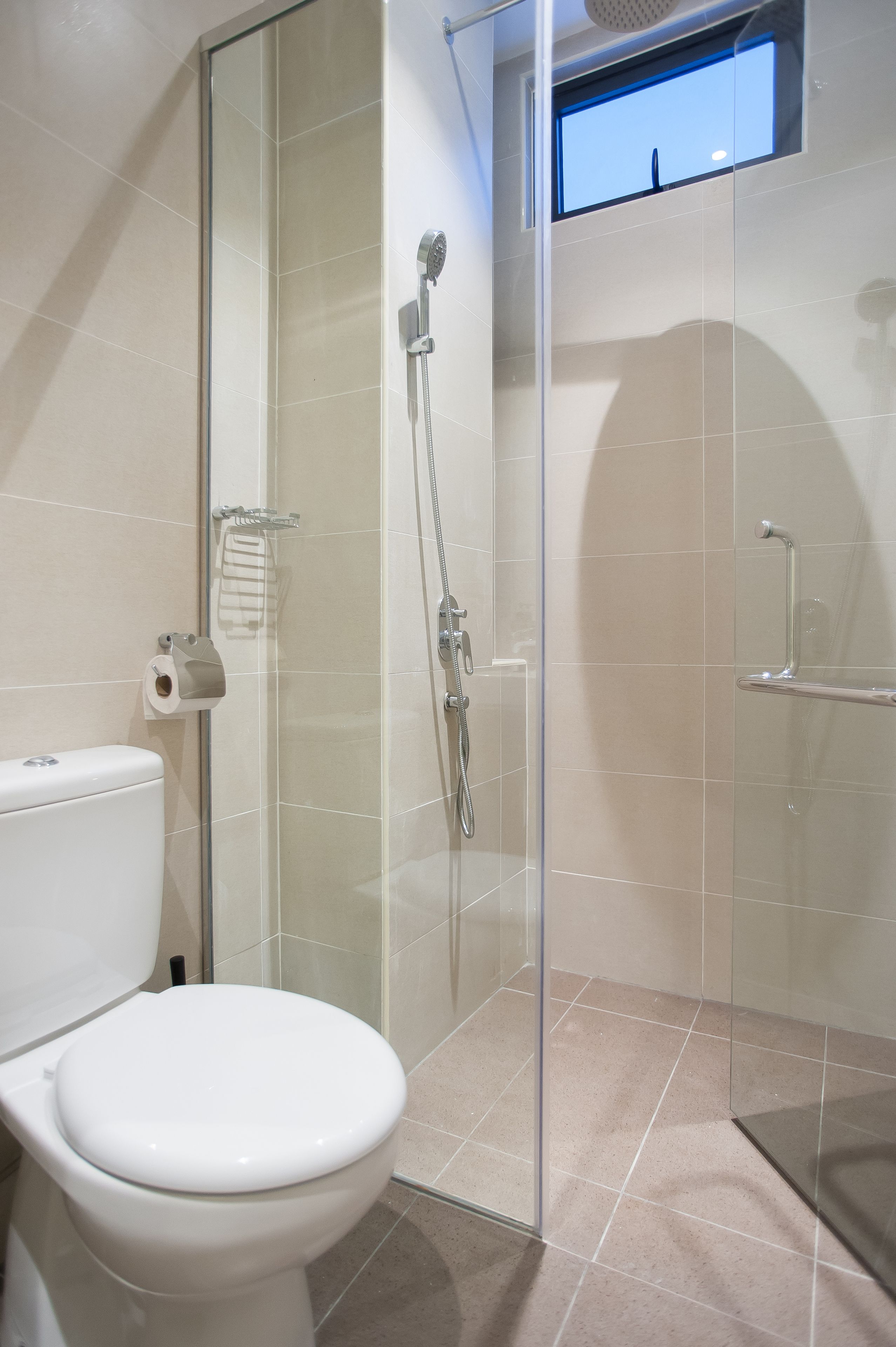 A modern bathroom with a glass-enclosed shower, a toilet, and a small window above the shower.