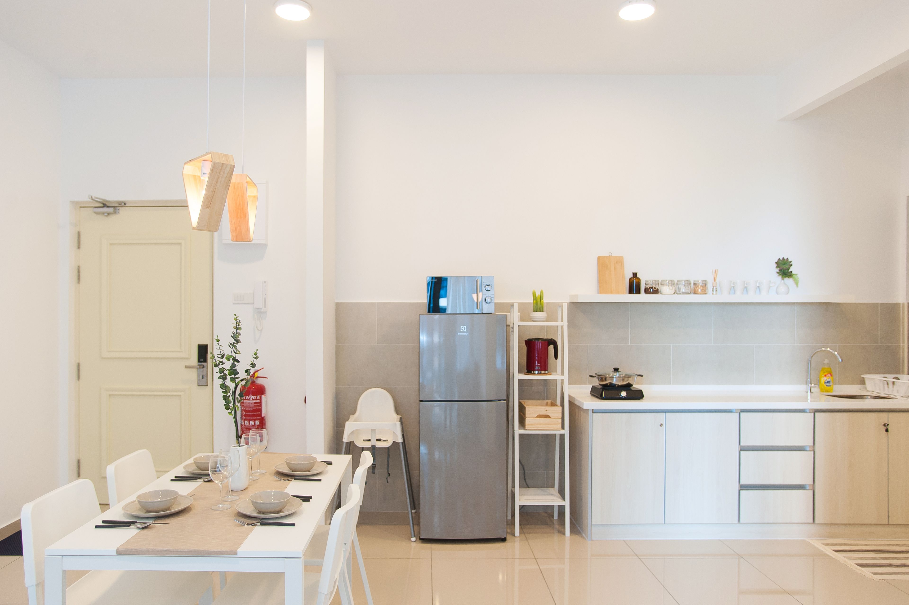 A modern kitchen with white cabinetry, a stainless steel refrigerator, and a dining area with a white table set for four.