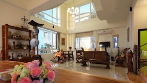 A spacious living room with high ceilings, large windows, a wooden coffee table, a television, and a chandelier. - Taroko Bay B&B (Xincheng)