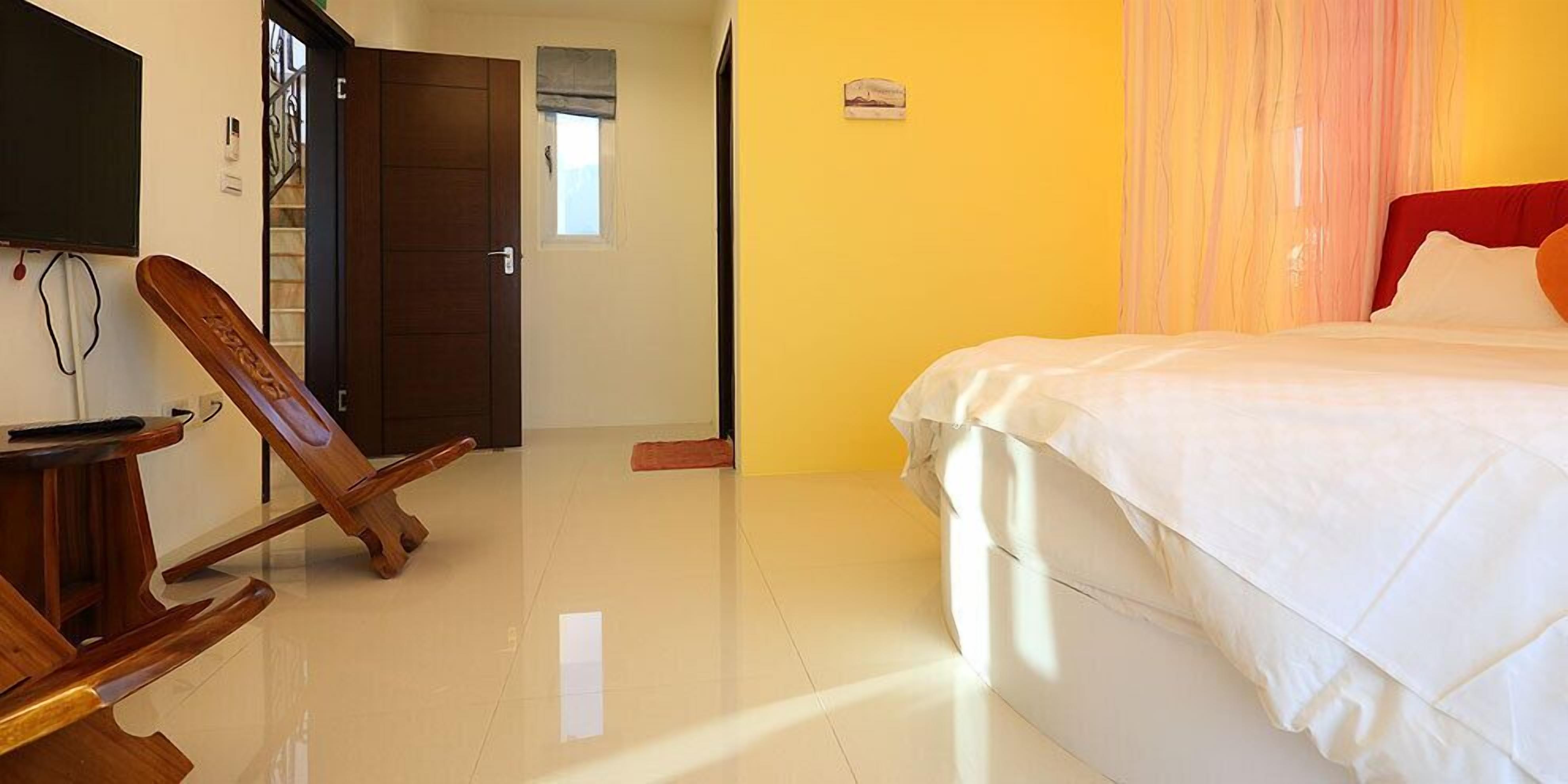 A hotel room with a bed, a wooden chair, a television, and a door leading to another room.