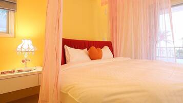 A bed with a red headboard, white and orange pillows, and sheer curtains.