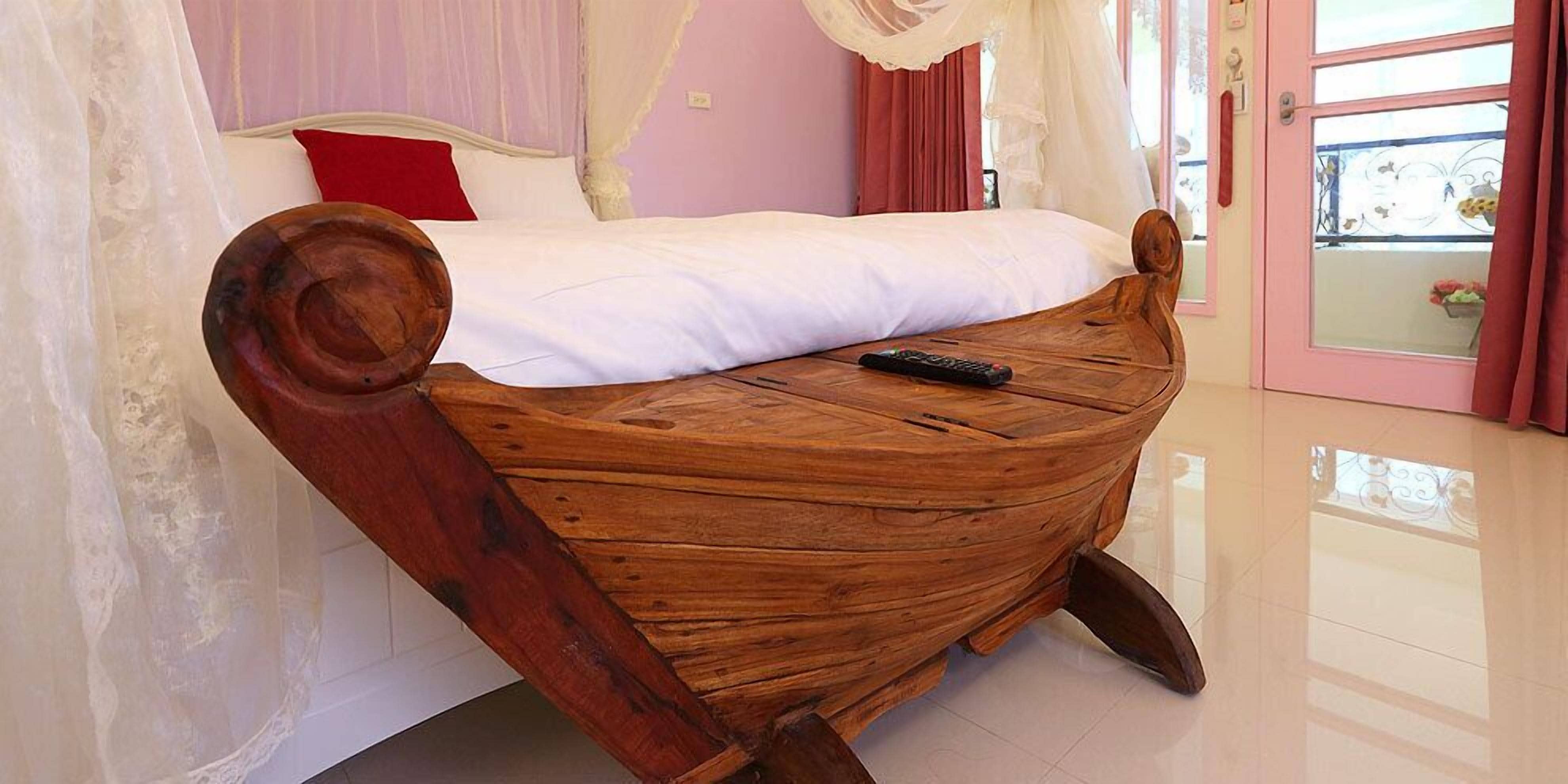 Una cama de madera con forma singular en una habitación con pared rosa, ropa de cama blanca y un control remoto sobre la cama.