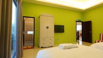 A hotel room with a green wall, a white wardrobe, a bed with white bedding, a TV mounted on the wall, and a door leading to another room.