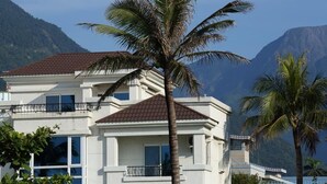 A multi-story building with a red-tiled roof, white walls, and balconies. It is surrounded by palm trees and mountains in the background. - Taroko Bay B&B (Xincheng)