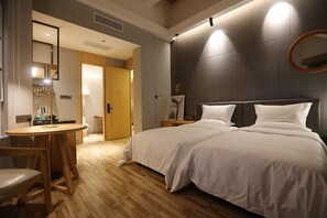 Una habitación de hotel con piso de madera, una cama con ropa blanca, una mesita con sillas y un espejo en la pared.
