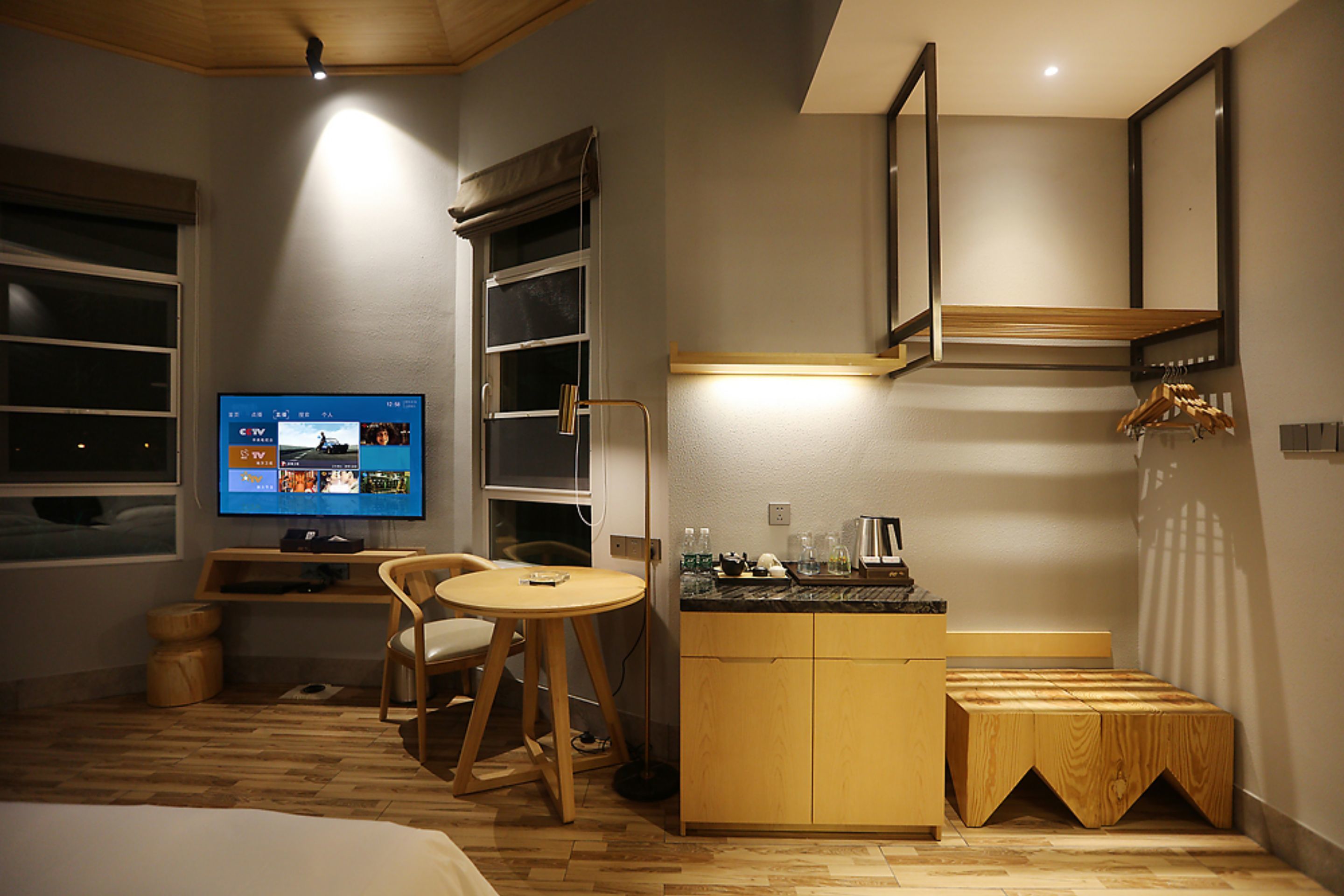 A compact hotel room with a bed, a small dining table, a TV, and a kitchenette.