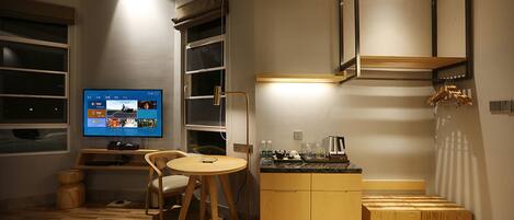 A compact hotel room with a bed, a small dining table, a TV, and a kitchenette.