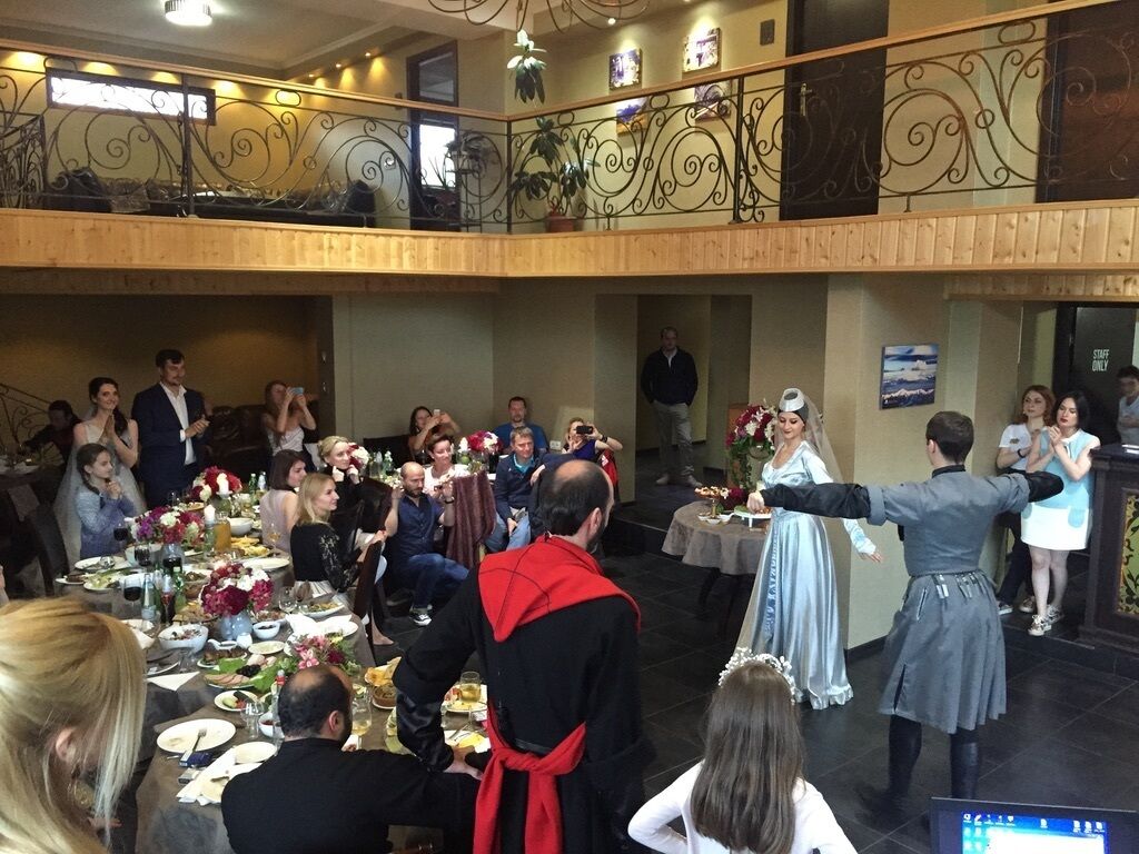 Un salón de banquetes con mesas dispuestas para un evento formal, un escenario con artistas y un balcón con vistas al salón.