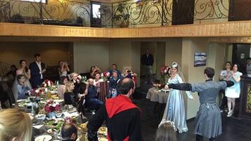 Un salón de banquetes con mesas dispuestas para un evento formal, un escenario con artistas y un balcón con vistas al salón.