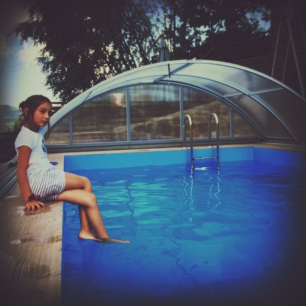 Una persona sentada junto a una piscina con cerramiento de vidrio.