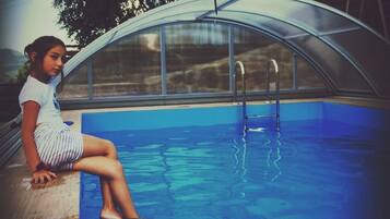 Una persona sentada junto a una piscina con cerramiento de vidrio.