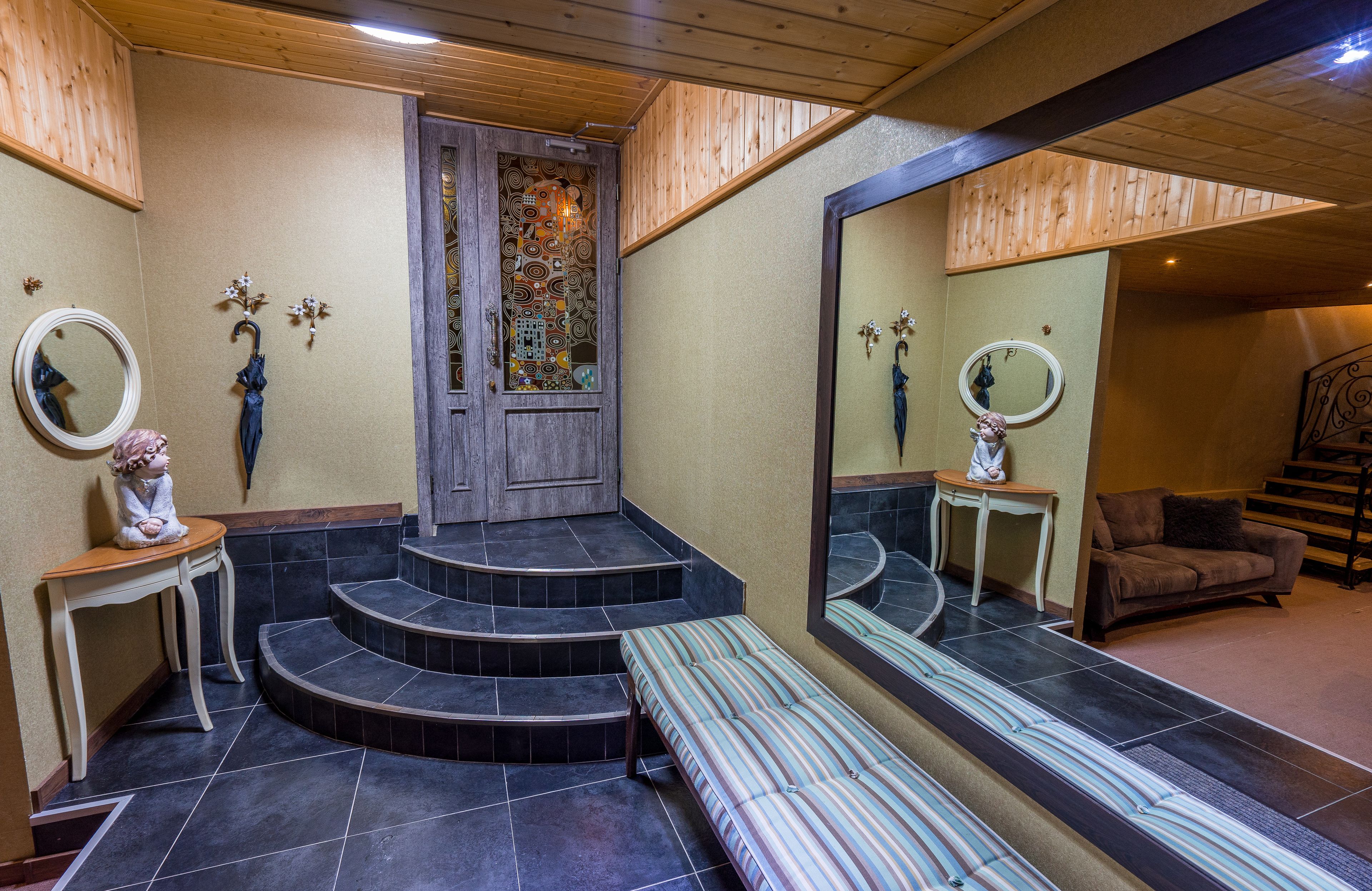 A bathroom with a wooden ceiling, a mirror, a bench, and a staircase leading to a door with a stained glass window.
