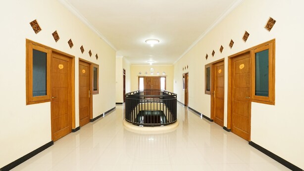 A hallway with wooden doors, a central staircase, and a ceiling light. - OYO 302 Karolin Homestay (Malang)