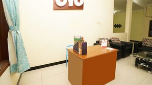 A reception area with a wooden desk, a blue chair, and a black sofa with patterned cushions. - OYO 302 Karolin Homestay (Malang)