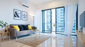 Een moderne woonkamer met een grijze bank, gele en zwarte kussens, een klein rond tafeltje en een grote glazen schuifdeur naar een balkon met uitzicht op de stad.