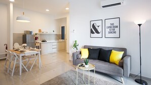Een moderne woonkamer met een grijze bank, gele kussens, een klein rond tafeltje met een plant en een eethoek met een witte tafel en stoelen.