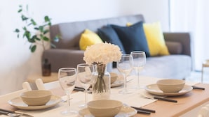 Een eettafel gedekt met witte borden, kommen en wijnglazen, een vaas met witte bloemen, en een kandelaar.