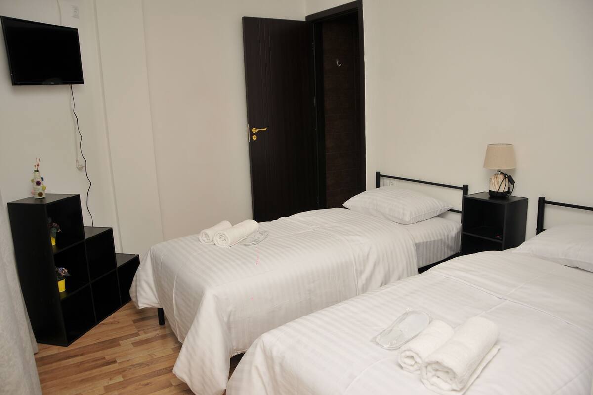 Habitación de hotel con dos camas, televisión, escritorio con lámpara y estante con adornos.