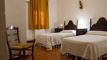 Un dormitorio con dos camas individuales, una silla de madera, una mesita de noche con una lámpara y una ventana con cortinas amarillas.