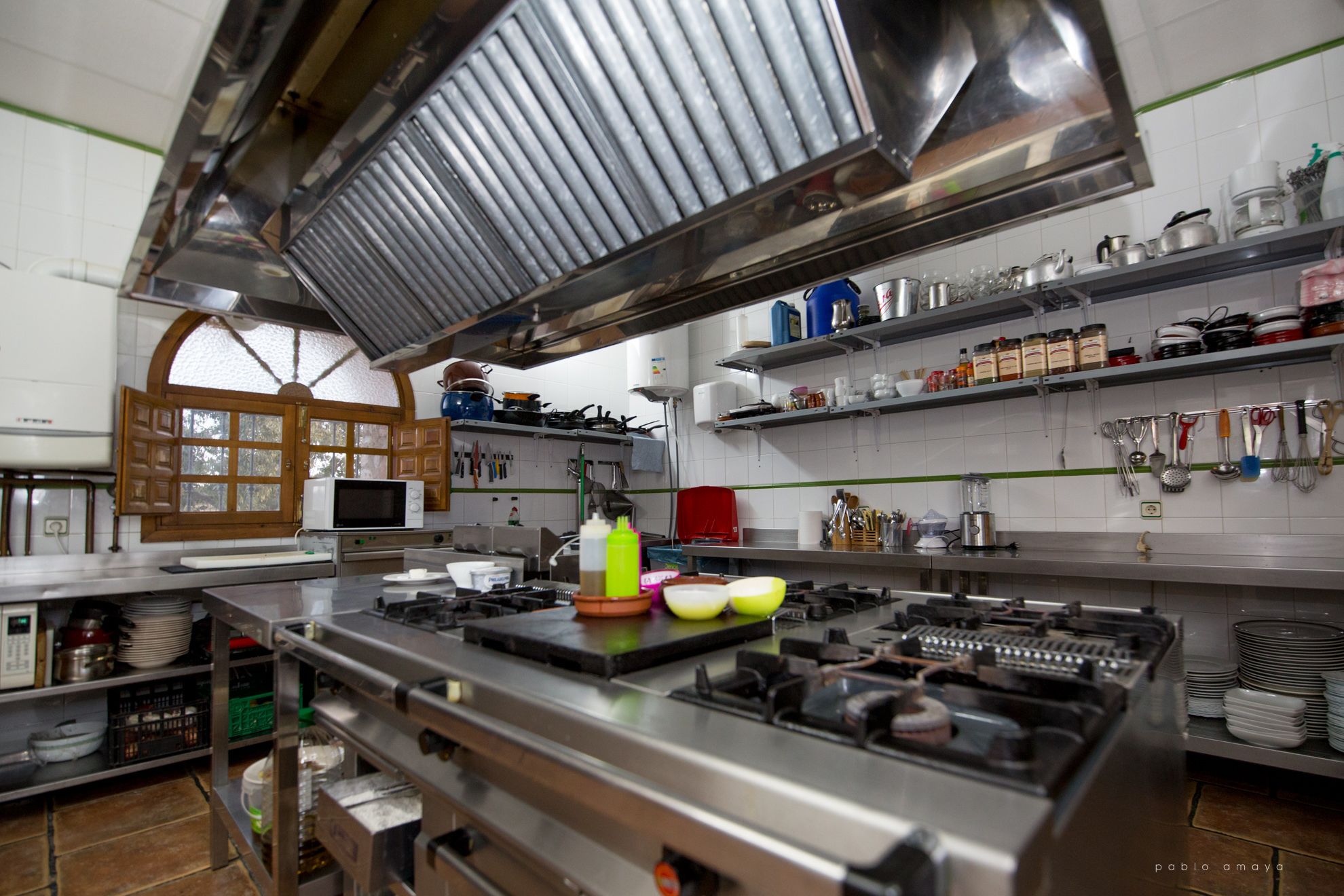 A kitchen with stainless steel appliances, a microwave, and various utensils on shelves.