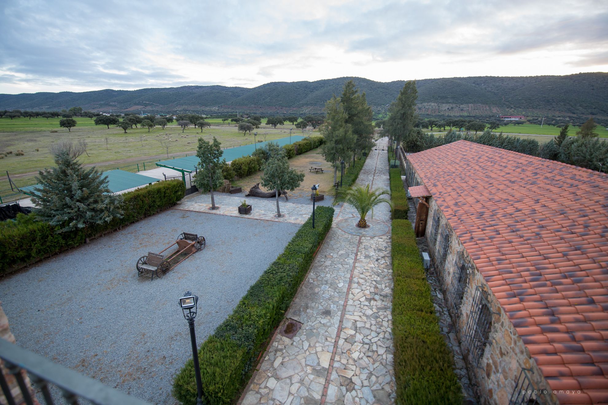 Un patio con un camino de piedra, un rincón de descanso y vistas a un campo verde y montañas a lo lejos.