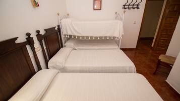 Un dormitorio con dos camas, cabeceros de madera, una mesita de noche pequeña, un perchero en la pared y un cuadro enmarcado.