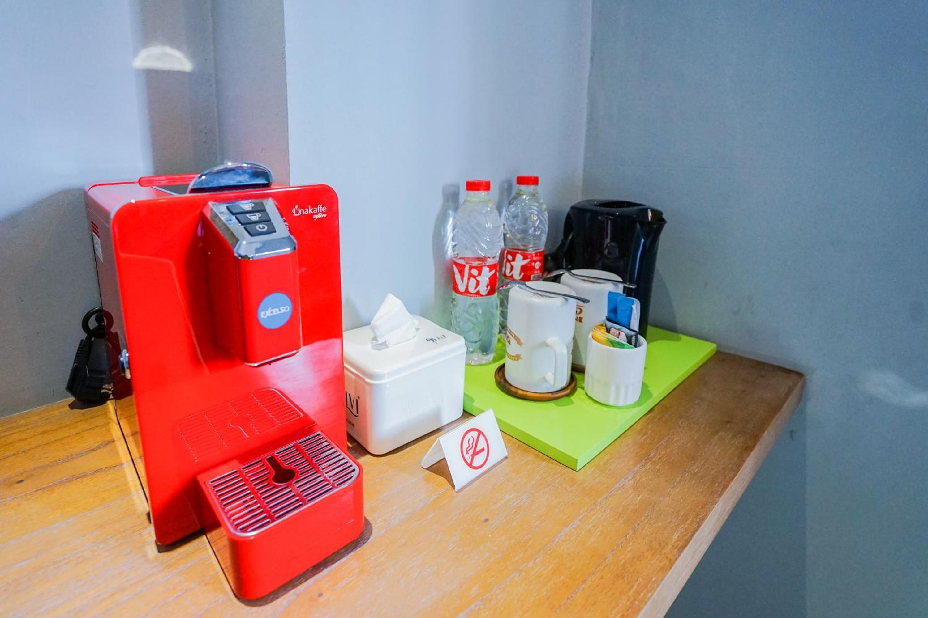 A coffee machine, two bottles of water, a tissue box, a coffee pot, and a small sign on a wooden table.