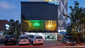 Et moderne hotel med en geometrisk facade, en synlig restaurant og en parkeringsplads med flere biler.