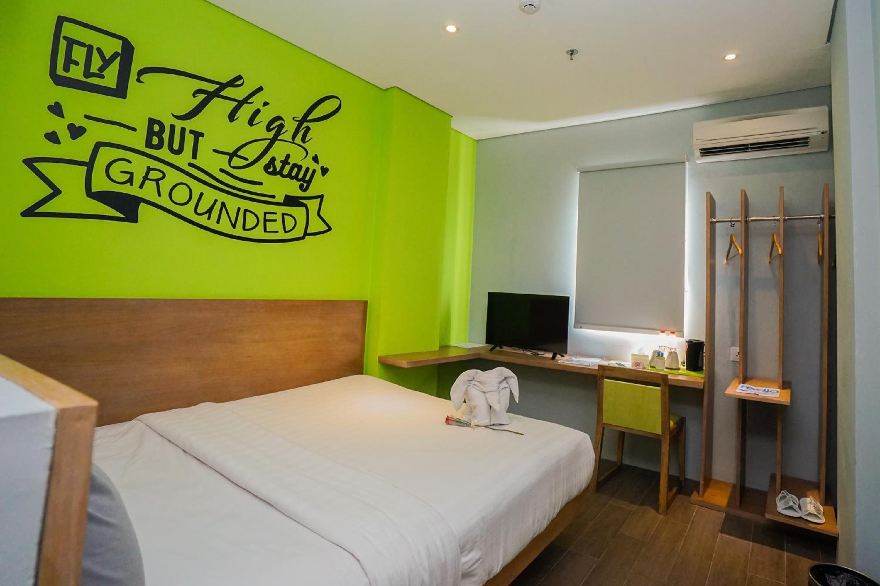 Habitación de hotel con cama, escritorio con computadora, televisión y pared con texto motivacional.