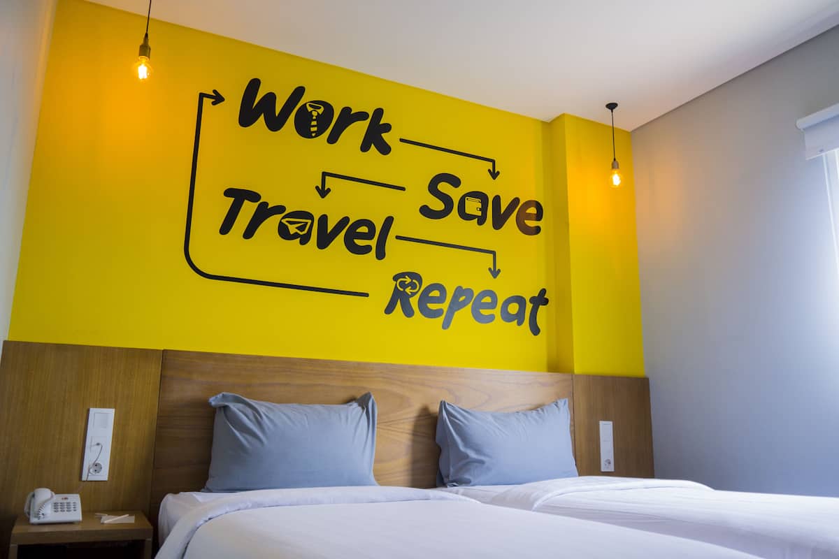 Une chambre d’hôtel avec un lit, une table de chevet et un mur orné d’un texte motivant.