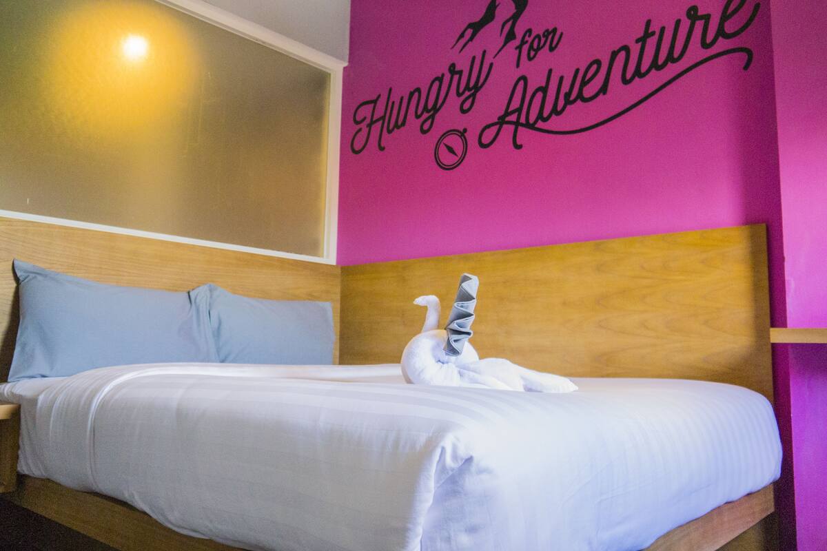Une chambre d’hôtel avec un lit, une tête de lit en bois et un mur orné d’une citation inspirante.