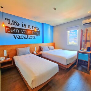 A hotel room with two beds, a wall quote, a window, and a small table with a lamp. - Radja Art and Boutique Hotel Simpang Lima (Semarang)