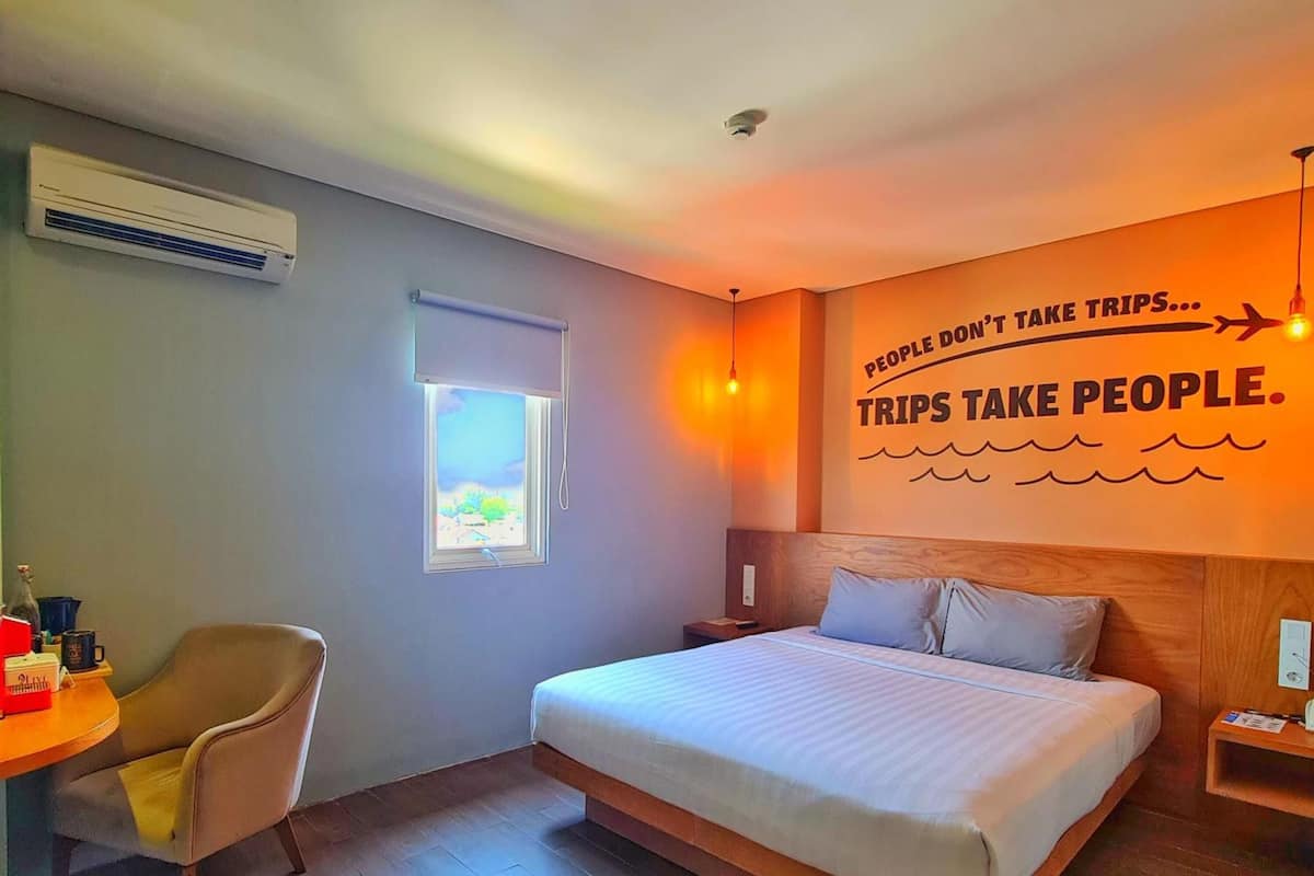 Une chambre d’hôtel comprenant un lit, un bureau, une chaise, une fenêtre et un mur orné d’une citation inspirante.