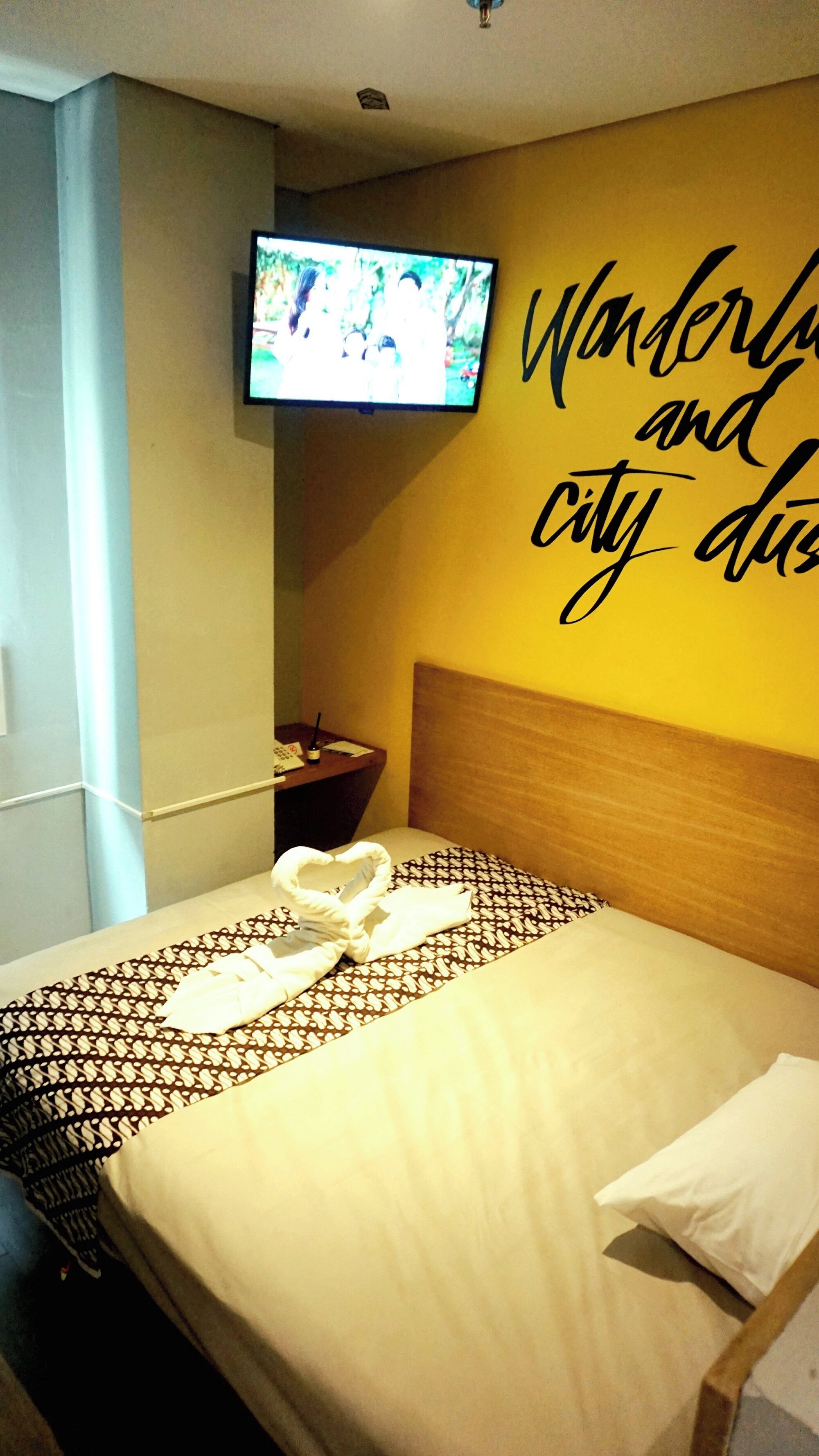 A hotel room with a bed, a TV mounted on the wall, and a wall with text.
