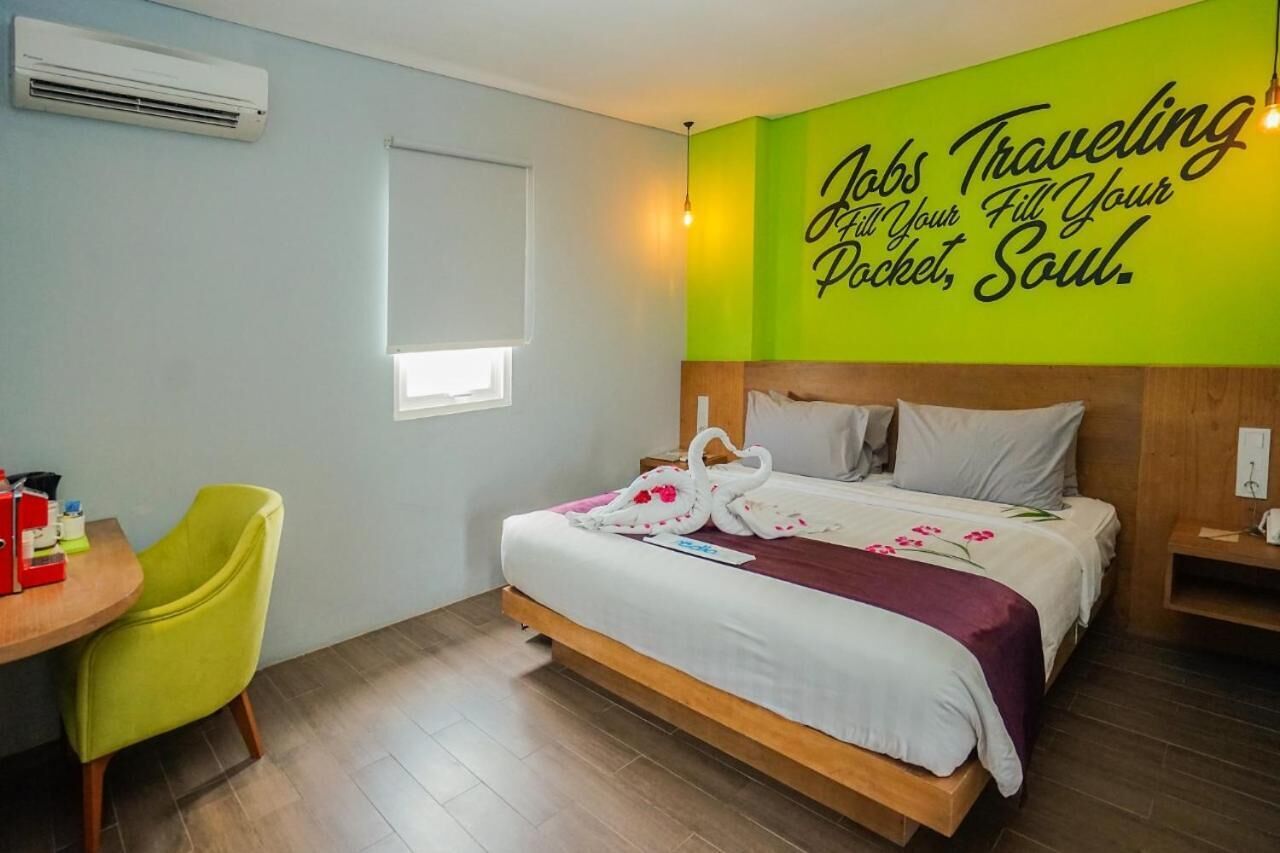Habitación de hotel con cama, escritorio, silla y pared con texto motivacional.