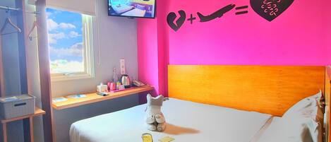 A hotel room with a bed, a desk, a TV, and a wall decoration.
