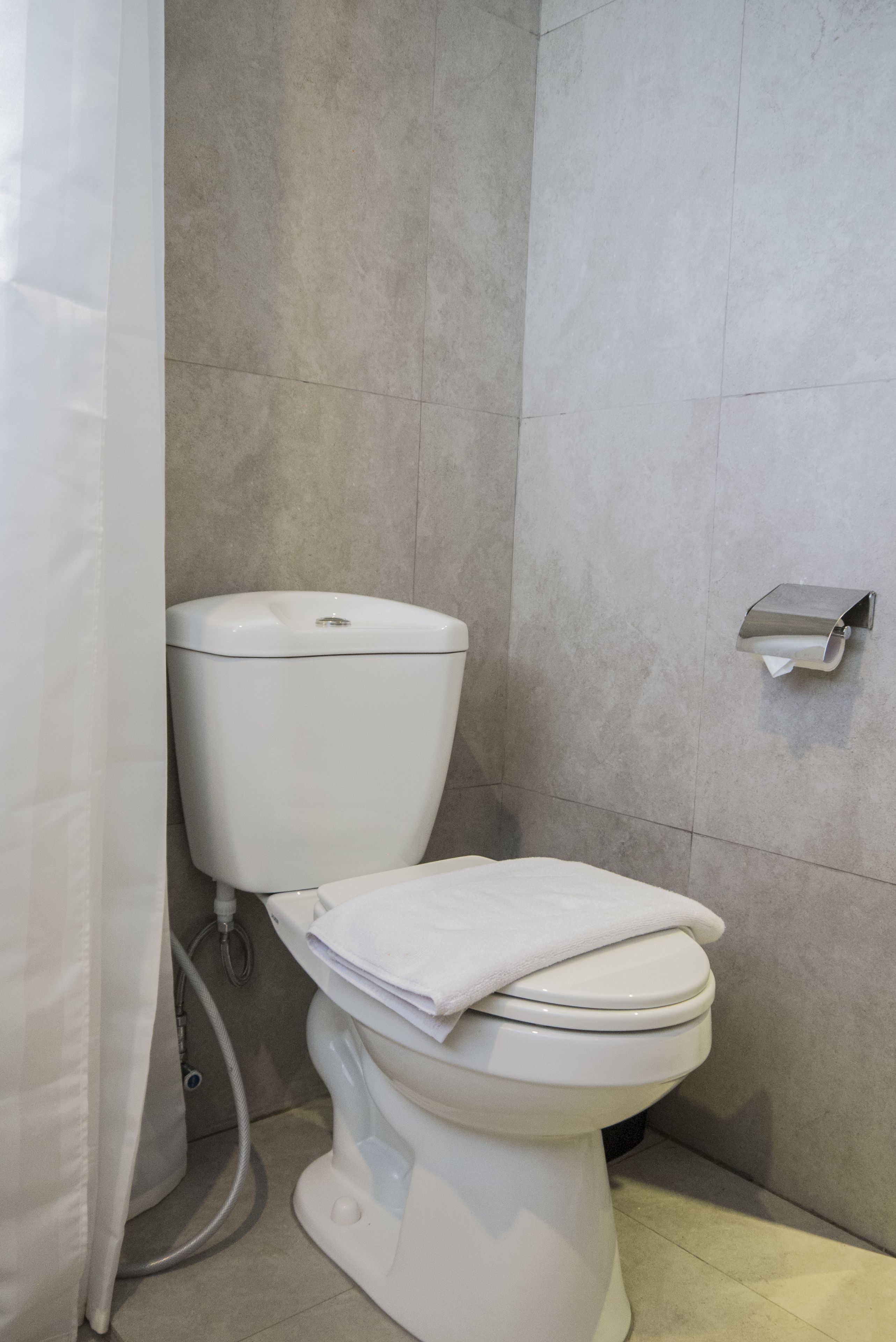 Un baño moderno con inodoro blanco, dispensador de toallas de papel y cortina de ducha.