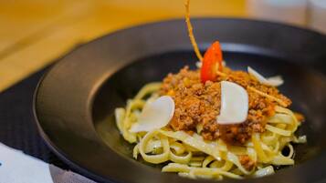A plate of spaghetti with a meat topping and a cherry tomato garnish.