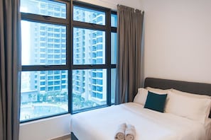 A hotel room with a large window, a bed with white linens, and a view of high-rise buildings. - A4 COZY Atlantis Family Suites 4-6pax-Pool View-Jonker (Malacca City)
