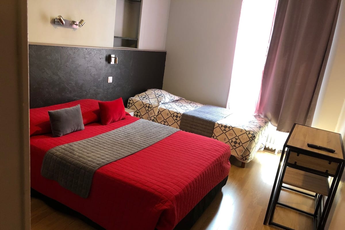 Una stanza con un letto grande, un letto più piccolo, un comodino e uno specchio.