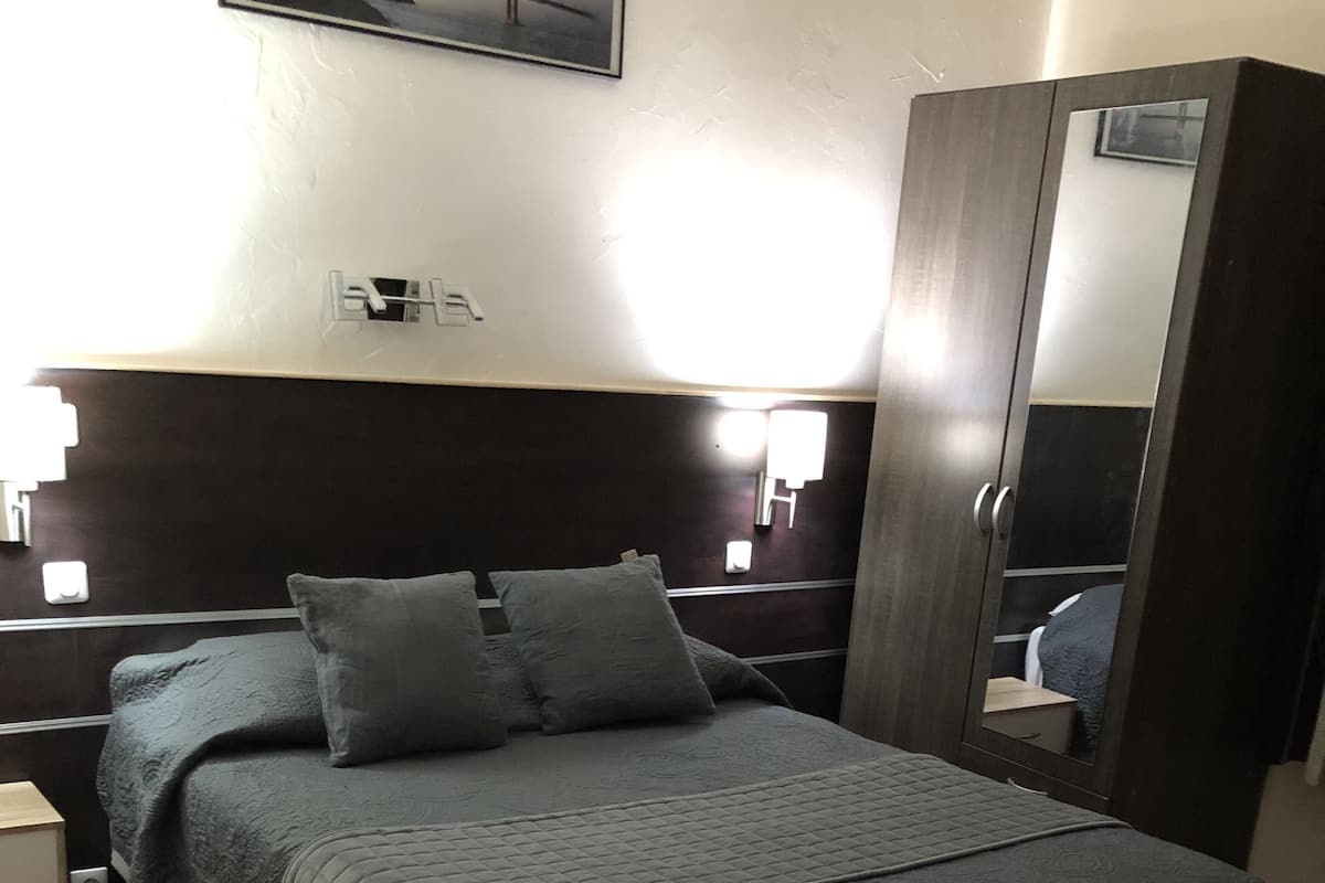 Una camera d'albergo con un letto, un comodino, una cassettiera, uno specchio e un quadro appeso al muro.