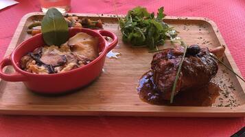 Un repas composé d’un plat servi dans un bol rouge, d’un steak et de légumes verts, le tout présenté sur une planche en bois.