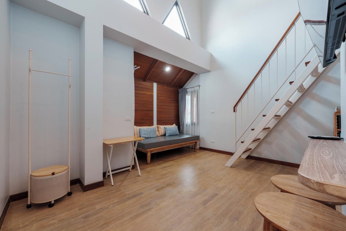 A modern interior with a loft-style bedroom, wooden flooring, a staircase, and a small seating area.